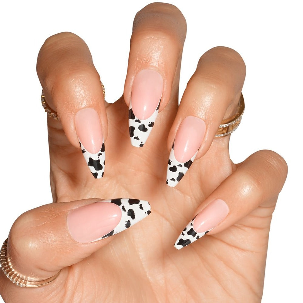 Hand in claw pose wearing cow printed French tip stick on nails