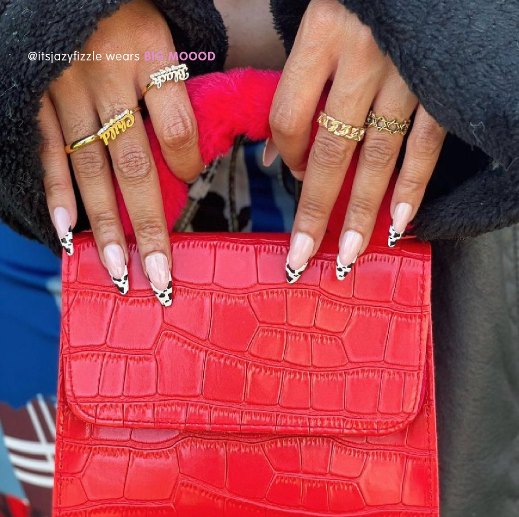 Influencer poses hands wearing Tres She cow print French tip instant acrylic press on nails over red bag