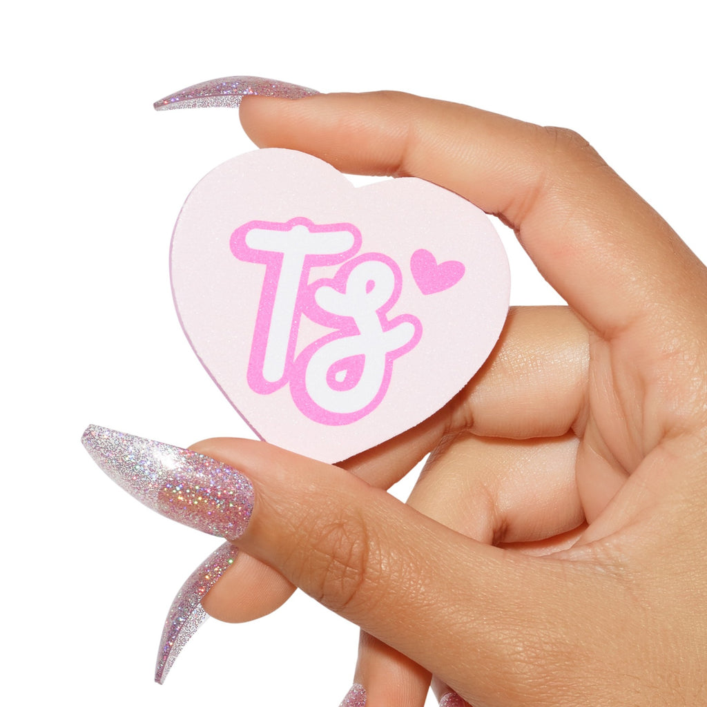 Hand holding heart shaped nail buffer with Tres She monogram in pink